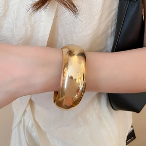 Bracelet manchette large doré poli avec finition miroir brillante sur le poignet du modèle