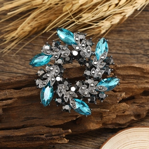 Blue rhinestone flower brooch with dark metal leaves on rustic wood surface