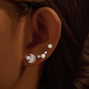 Macro shot of silver crescent moon and pearl earring set worn on the earlobe