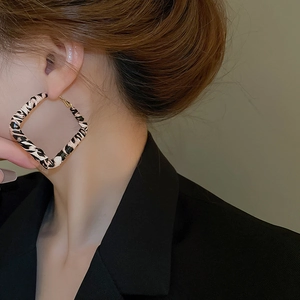 Close-up of leopard print oversized square earrings worn with a chic black blazer