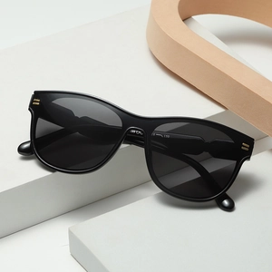 Modern oval black sunglasses with gold hinges displayed on white geometric stones