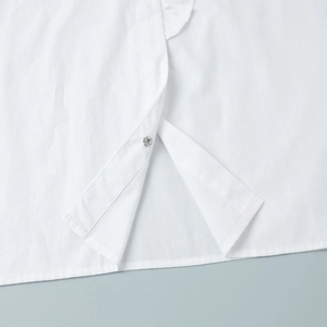Detailed close-up of white cotton shirt hem with silver metal snap button and neat stitching