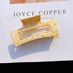 Detail of matte cream acrylic hair claw clip with orange ink pattern and hollow design