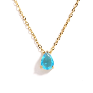 Macro detail of gold O-chain necklace with a teardrop blue zircon pendant in claw setting