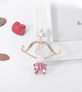 Detailed close-up of bow and arrow brooch with pink crystals, pearls, and zircons