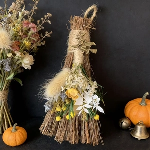 Detail of a decorative Halloween broom with dried flowers, leaves and a metal witch charm