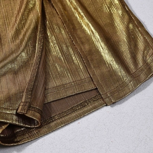Detailed close-up of metallic gold pleated fabric texture with neat hemline stitching
