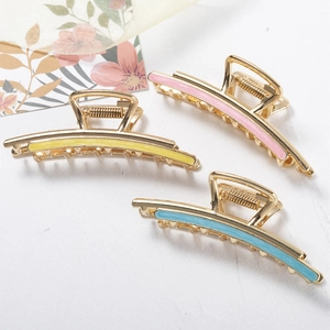 Three elegant gold metal hair claws with colorful enamel stripes on a white surface