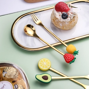 Golden stainless steel fruit-topped dessert spoon and fork set on a marble tray