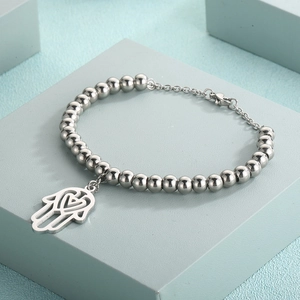 Detail of silver beaded bracelet featuring a hollow heart Hamsa hand charm on a blue stand