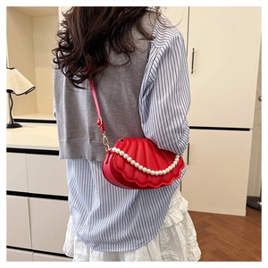 Detail showing red shell-shaped crossbody bag with pearl chain decoration on model