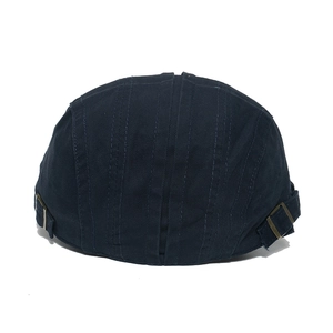 Detail of dark canvas flat cap featuring bronze metal side buckles and reinforced stitching
