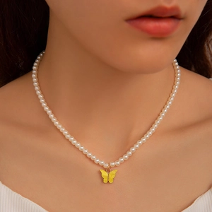 Detail of elegant pearl necklace featuring a vibrant yellow butterfly pendant on a model