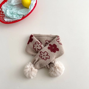 Detail of beige knitted kids scarf featuring red floral patterns and plush pom-poms