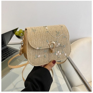 Detail of beige straw saddle bag featuring floral embroidery and gold metal clasp