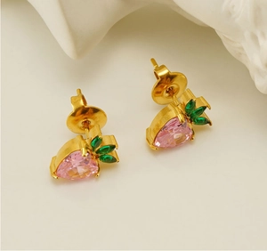 Macro detail of strawberry-shaped gold studs with pink heart stones and green leaves