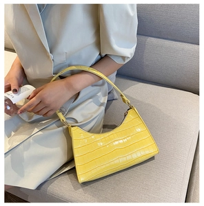 Detailed view of yellow crocodile embossed texture handbag carried on a model shoulder