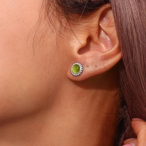 Close-up of woman wearing a round silver earring with green cat eye stone and beaded edge