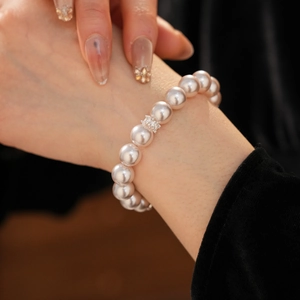 Détail macro du bracelet élégant en perles blanches rondes avec breloque fleur en zircon