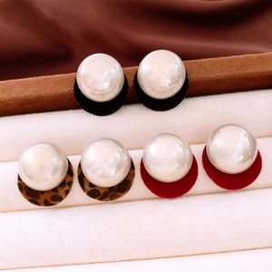 Macro detail of three pearl stud earrings with black, leopard, and red flocked base pads