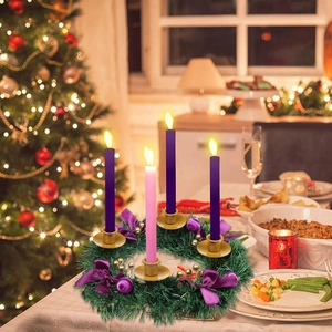 Advent wreath with four lit candles, purple bows and gold berries on festive table