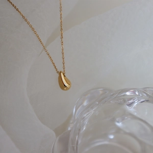 Primo piano artistico di una collana con ciondolo a goccia in oro 18K su tessuto bianco