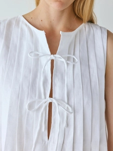Détail d'une robe courte blanche sans manches avec plis verticaux et nœuds décoratifs