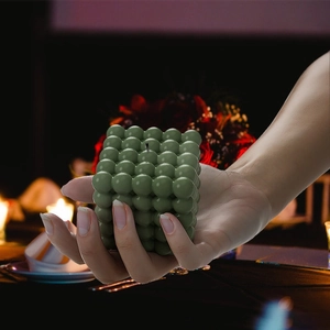 Mano che tiene una candela profumata a cubo verde in un ambiente da cena romantica
