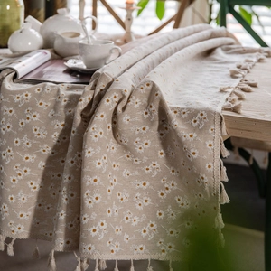 Linen cotton tablecloth with white daisy floral print and fringe edges on wooden table