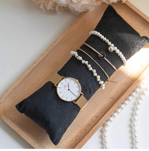 Detail view of gold mesh watch and pearl bracelets on black velvet display pillow