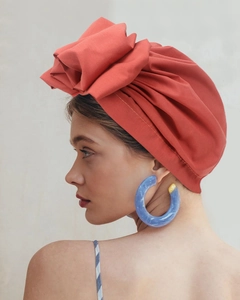 Detail of coral orange pleated turban hat with large 3D fabric flower and matching blue earrings