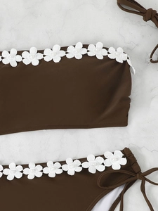 Detail of dark brown bikini with white 3D lace flowers and pearl beads on marble
