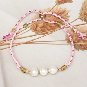Detail of pink and white braided rope bracelet with three white pearls and gold accents