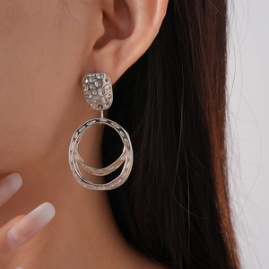 Détail de boucles d'oreilles géométriques argentées avec motifs carrés et circulaires