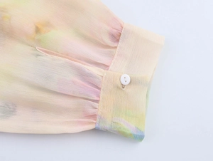 Dettaglio del polsino in chiffon con stampa tie-dye e bottone rotondo bianco