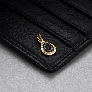 Macro shot of gold teardrop pendant with black pave settings on textured leather