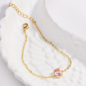 Detail of gold plated bracelet featuring a pink oval zircon on a white feather tray