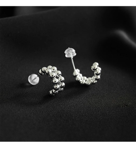 Macro detail of silver C-shaped beaded earrings with clear silicone safety backings
