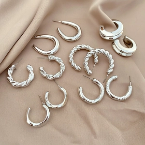 Close-up of assorted silver hoop earrings with twisted and smooth textures on silk