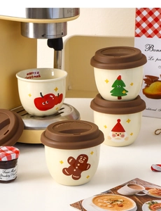 Close-up of mini Christmas ceramic mugs with gingerbread and Santa patterns near coffee maker