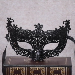 Detail of a black masquerade mask with glitter coating resting on vintage books