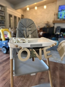 Detail of wooden 'ONE' letter banner and Christmas tree decor on baby high chair