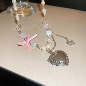 Détail du nœud rose et du médaillon cœur argenté sur un collier de perles et étoiles