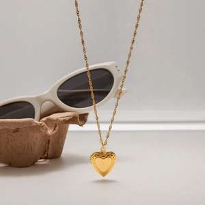 Detail of a golden heart-shaped locket necklace with embossed patterns on a twisted chain