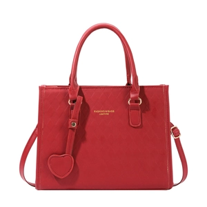 Red quilted leather tote bag with gold hardware and heart pendant on white background