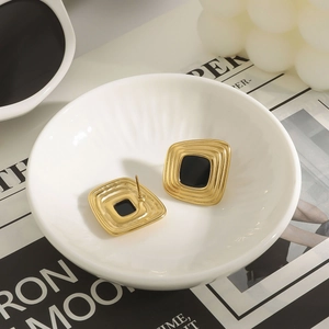 Macro detail of irregular gold and black resin stud earrings on a ceramic dish