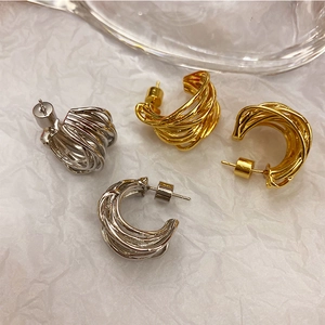 Detail of gold and silver wire-wrapped C-shape earrings on white textured background