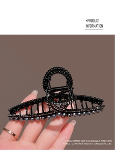 Detail of a black twisted hair claw clip with delicate bead accents held by hand