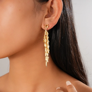 Detailed view of long gold tassel earrings with wheat leaf design on model