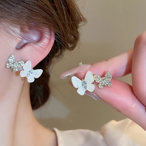 Vue détaillée des boucles d'oreilles papillon dorées avec cristaux et émail blanc